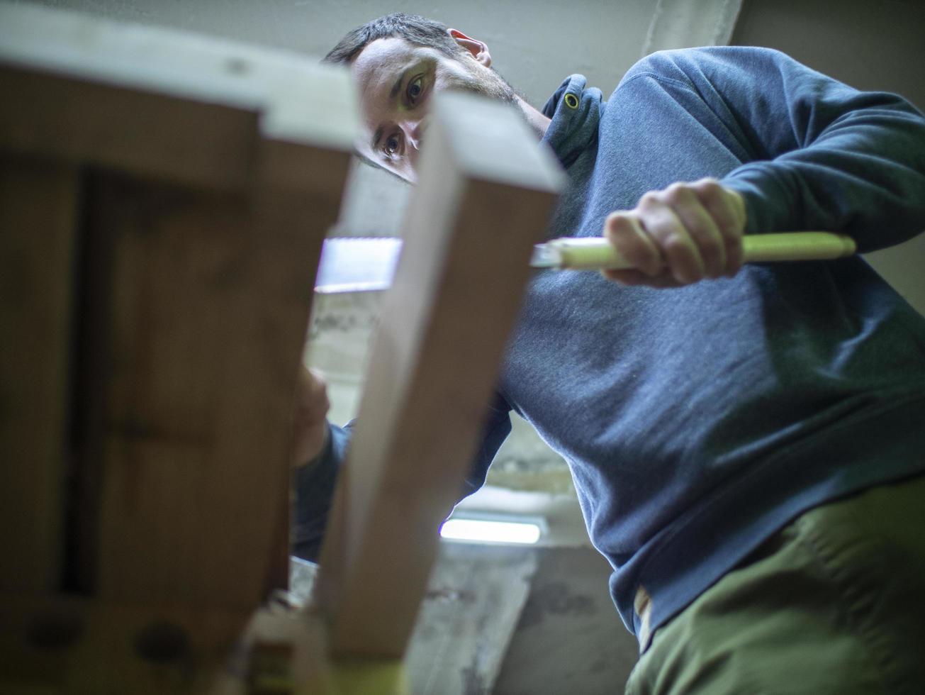 Holzarbeiter mit Bart, der mit einer Handsäge einen Holzbalken sägt. ein Zimmermann, der ein Stück Holz sägt. Ansicht von unten foto