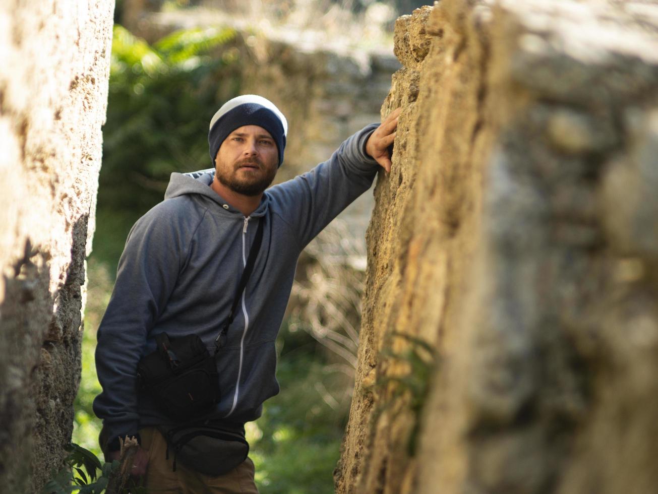 bärtiger Mann in Strickmütze und Jacke mit Kapuze posiert in einer Schlucht einer Festung foto