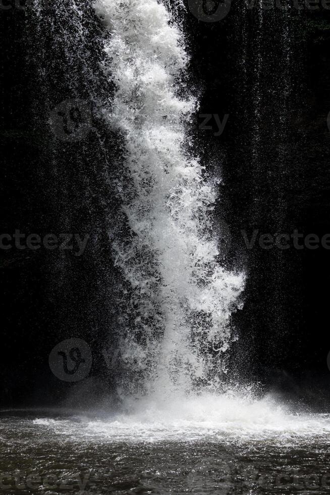 planschen Wasser von mächtig Wasserfall mit dunkel Hintergrund. foto