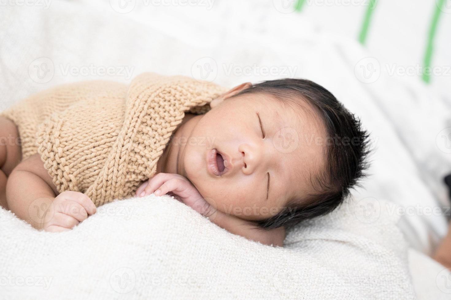 glückliches süßes entzückendes asiatisches Baby mit schwarzem Haar, das eine weiße Decke liegt foto
