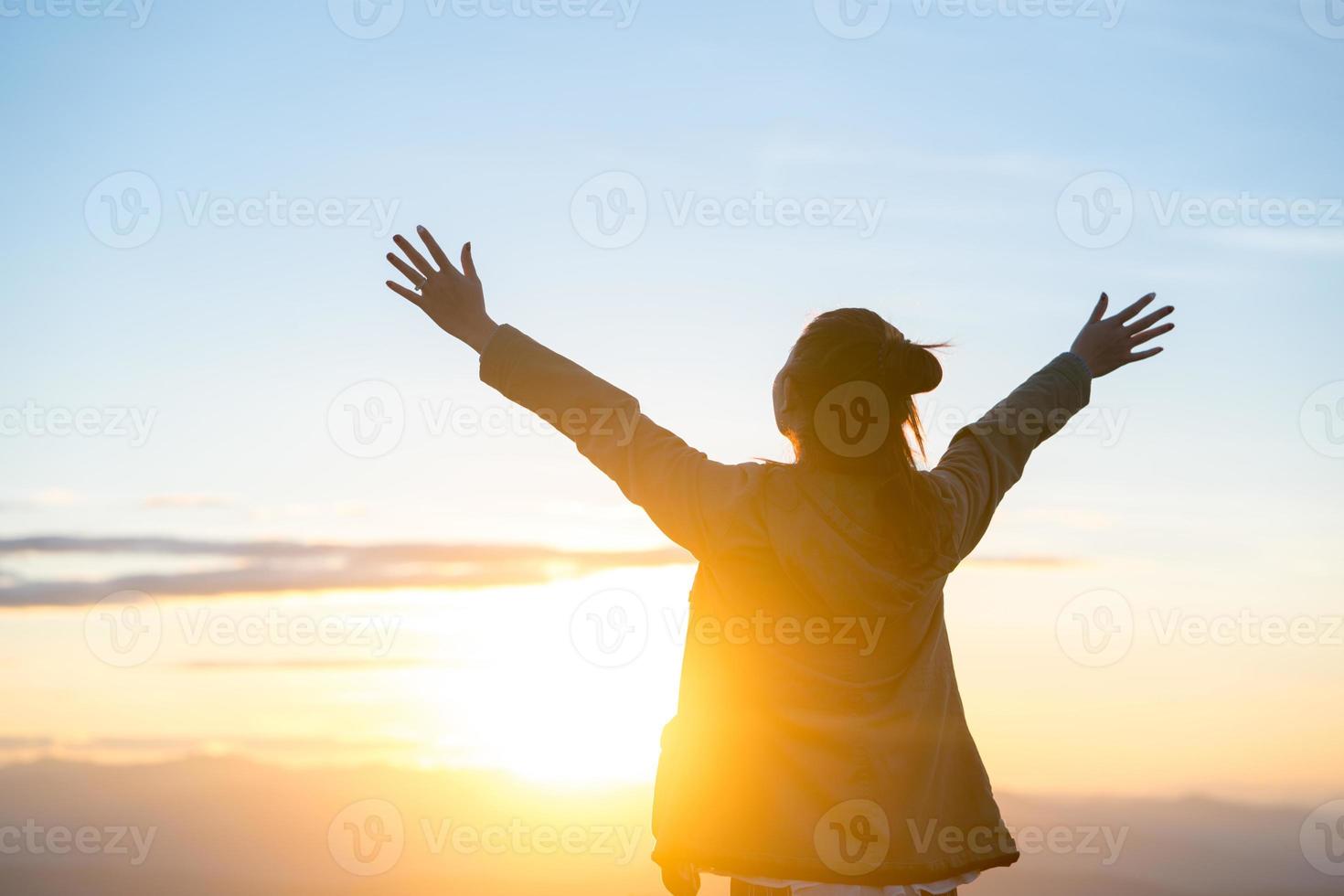 glückliche Frau, die allein mit erhobenen Armen bei schönem Sonnenaufgang am Morgen steht foto