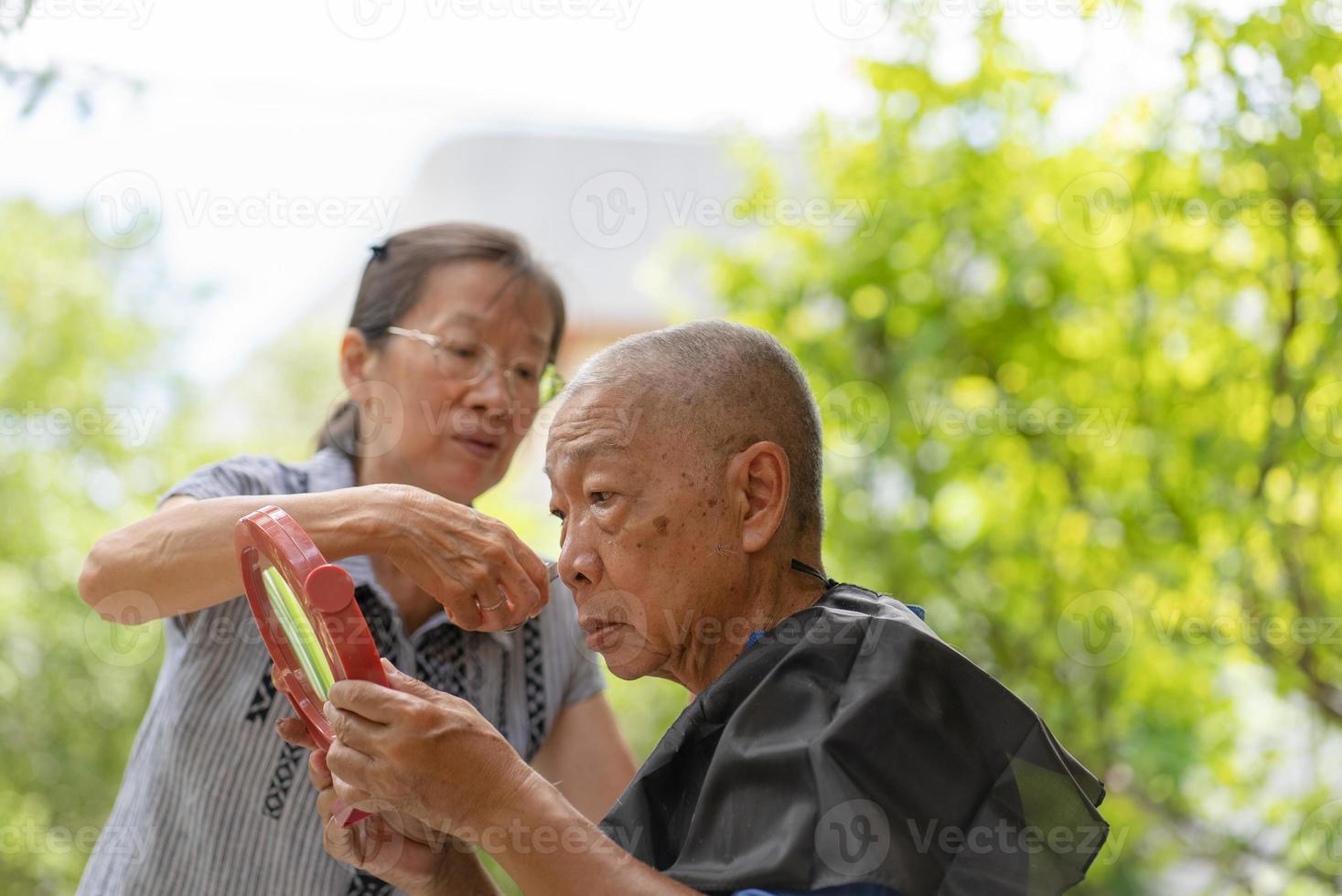 ältere asiatische frau, die ihrem mann auf der terrasse haarschnitt foto