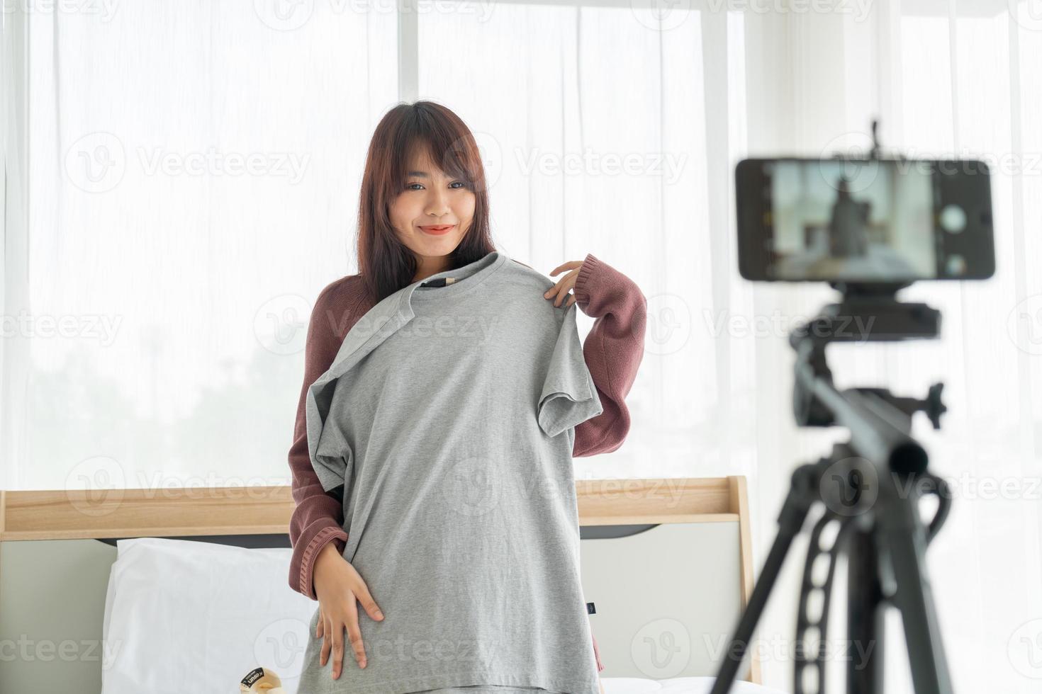 Schöne asiatische Bloggerin, die Kleidung vor der Kamera zeigt, um Vlog-Video-Live-Streaming in ihrem Geschäft aufzunehmen - Online-Influencer auf Social-Media-Konzept foto