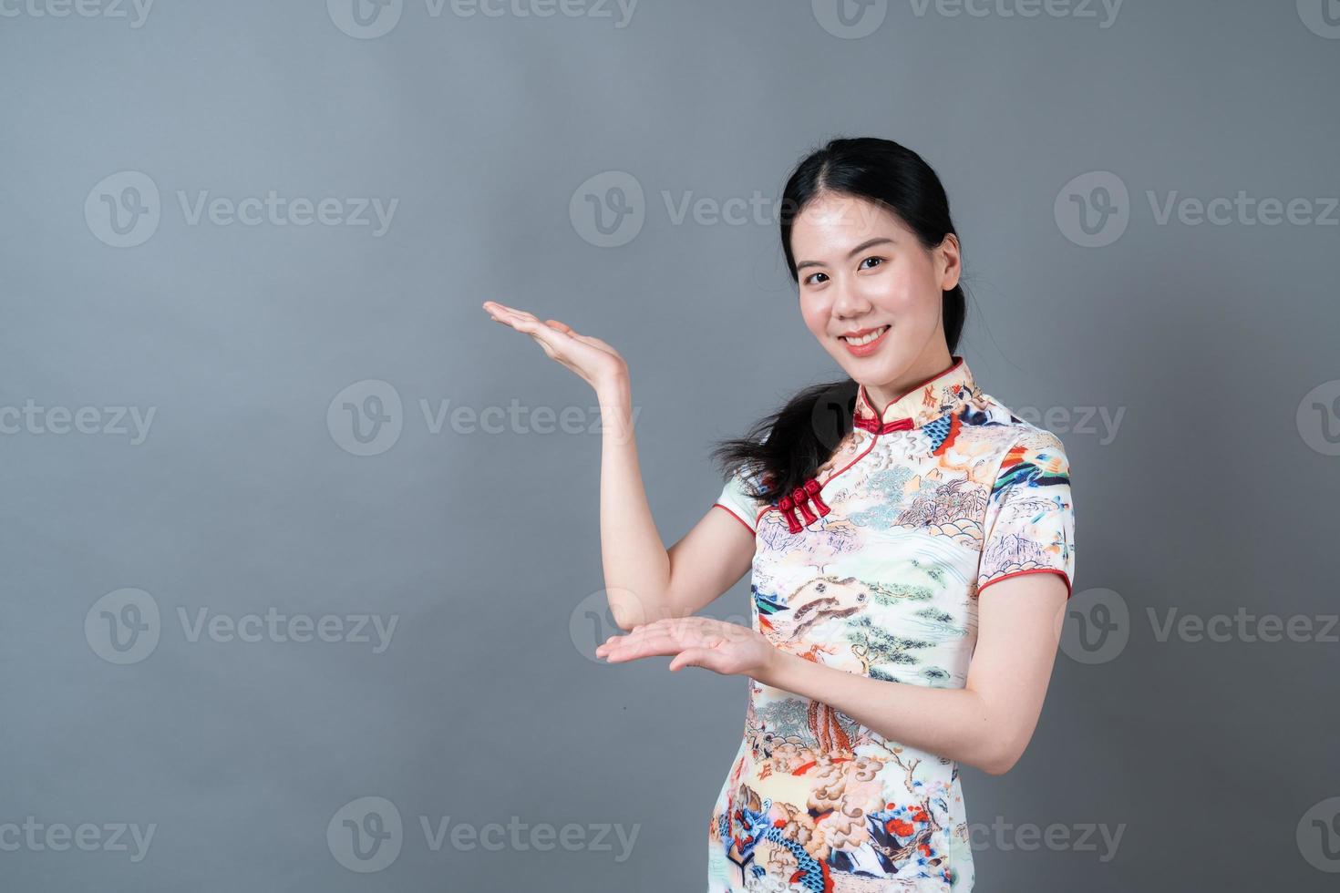 schöne junge asiatische frau trägt chinesisches traditionelles kleid mit der hand, die auf der seite präsentiert foto