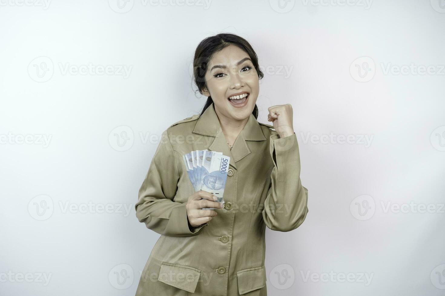 ein erfolgreich jung Regierung Arbeiter Frau ist tragen khaki Uniform halten Kasse Geld im indonesisch Rupiah isoliert durch Weiß Hintergrund foto