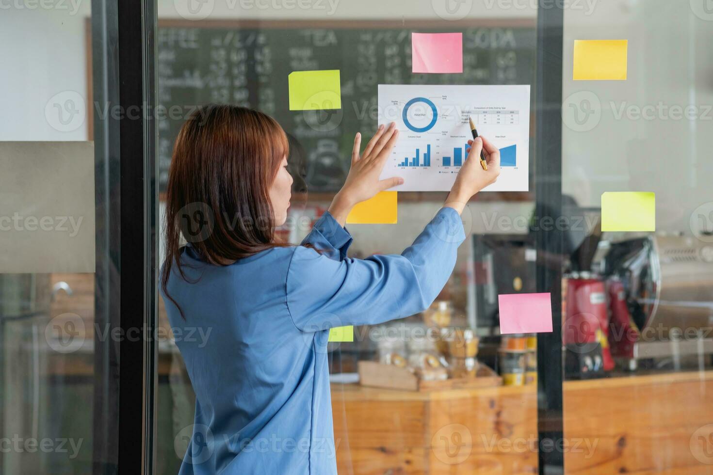 ein weiblich Mitarbeiter schreibt auf ein bunt Notizblock. ethnisch Frauen Arbeiten beim Startups Brainstorming Kollaborativ Pläne auf Glas Mauer Aufkleber sehen weniger. foto