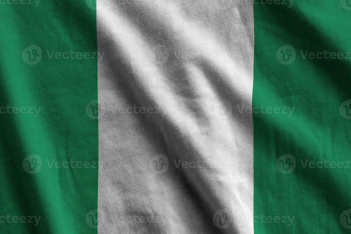 nigerianische flagge mit großen falten, die im innenbereich unter dem studiolicht wehen. die offiziellen symbole und farben im banner foto