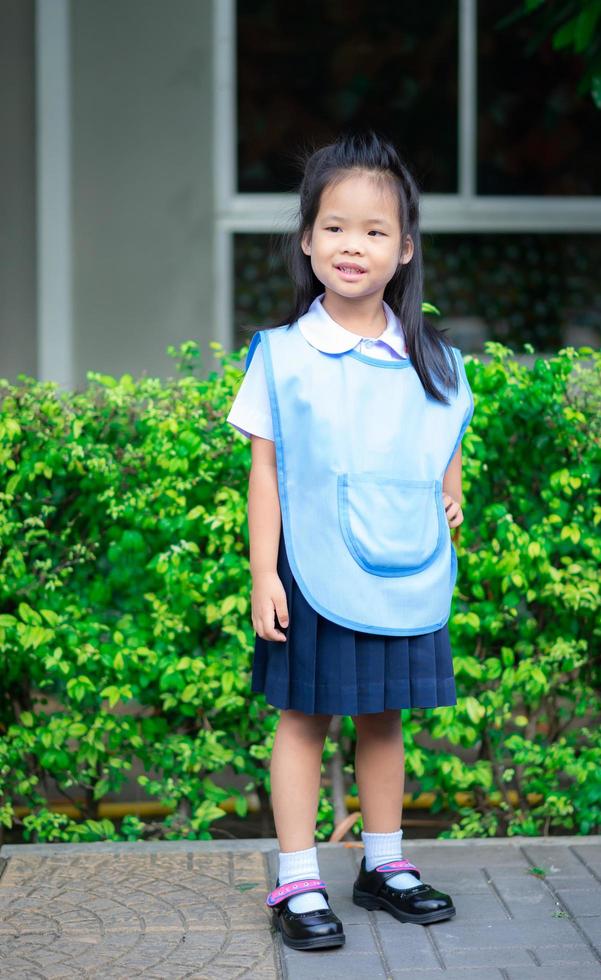 Porträt eines glücklichen kleinen Mädchens in thailändischer Schuluniform, das auf dem Fußweg steht, bereit zurück zur Schule foto