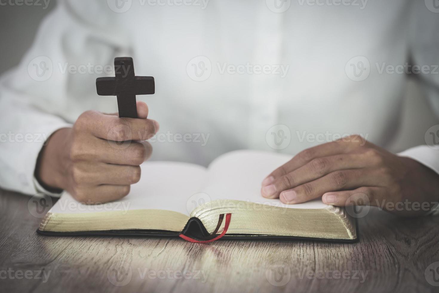 die Frau hält das Kreuz und betet mit ihren Schriften auf dem Tisch. foto