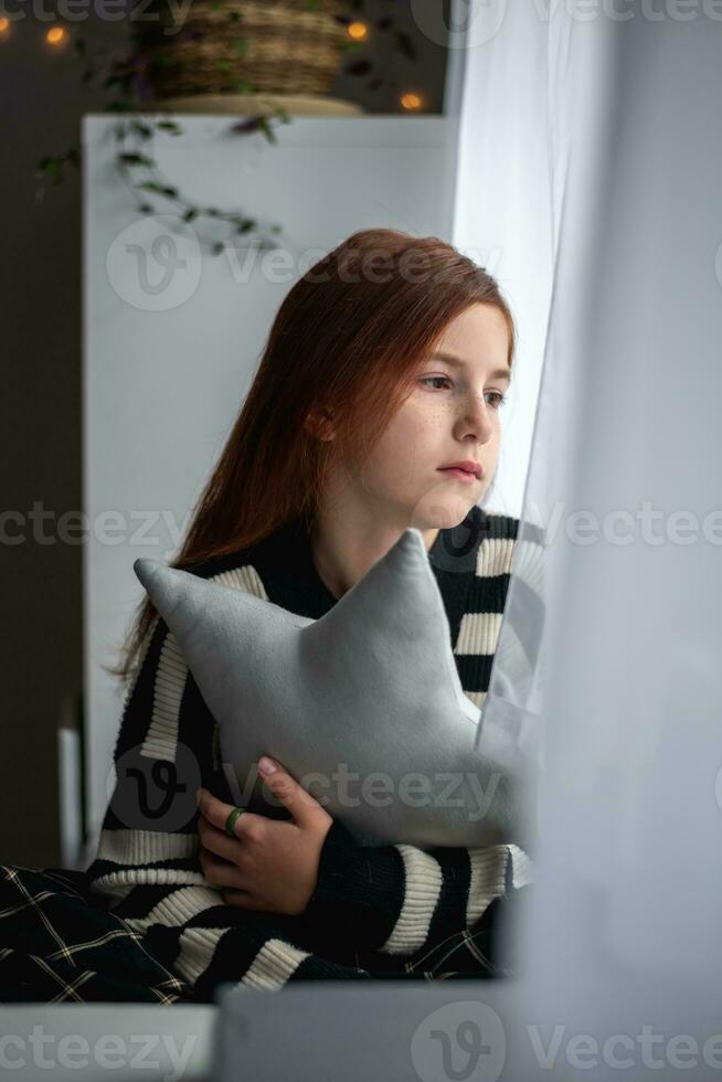 ein nachdenklich Teenager Mädchen sieht aus aus das Fenster. Nachdenklichkeit, Traurigkeit, Einsamkeit foto