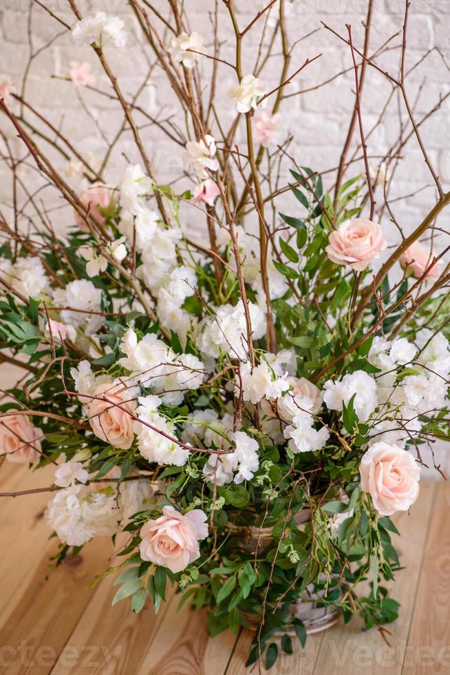 Dekorationen von Zweigen mit schönen rosa und weißen Blumen im Korb vor dem Hintergrund einer weißen Backsteinmauer foto