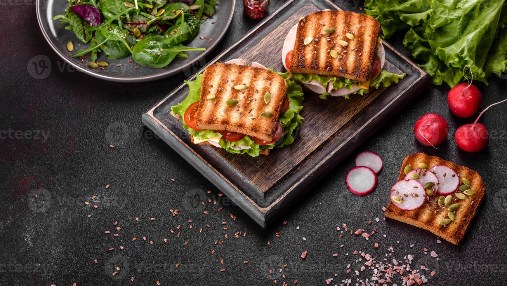 leckeres Sandwich mit knusprigem Toast, Schinken, Salat und Tomaten foto