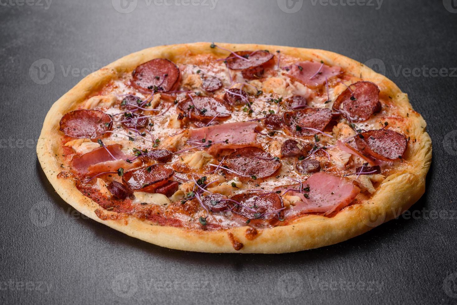 leckere frische Ofenpizza mit Tomaten, Salami und Speck auf dunklem Betongrund foto