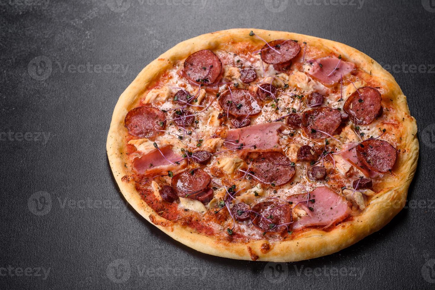 leckere frische Ofenpizza mit Tomaten, Salami und Speck auf dunklem Betongrund foto