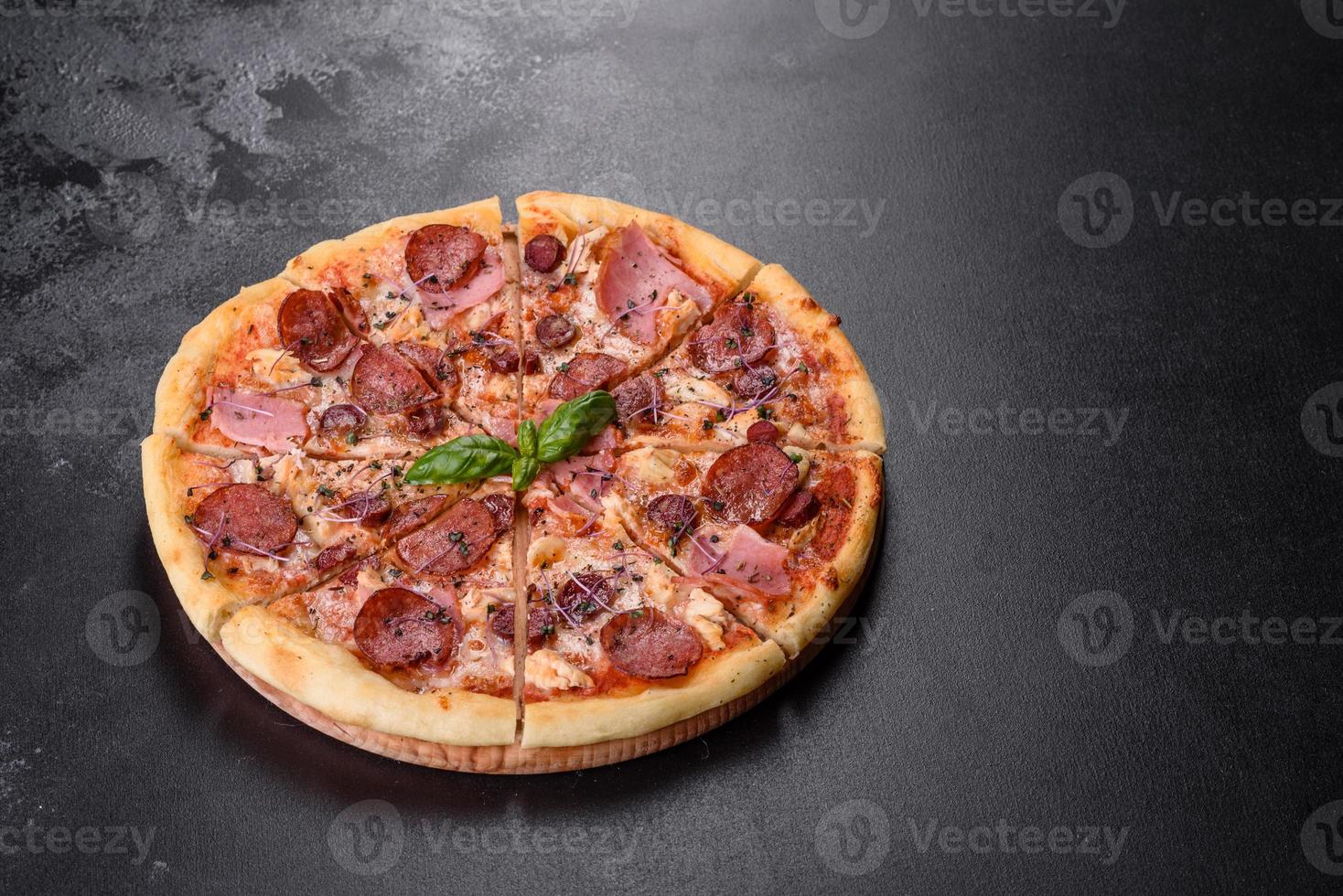 leckere frische Ofenpizza mit Tomaten, Salami und Speck auf dunklem Betongrund foto