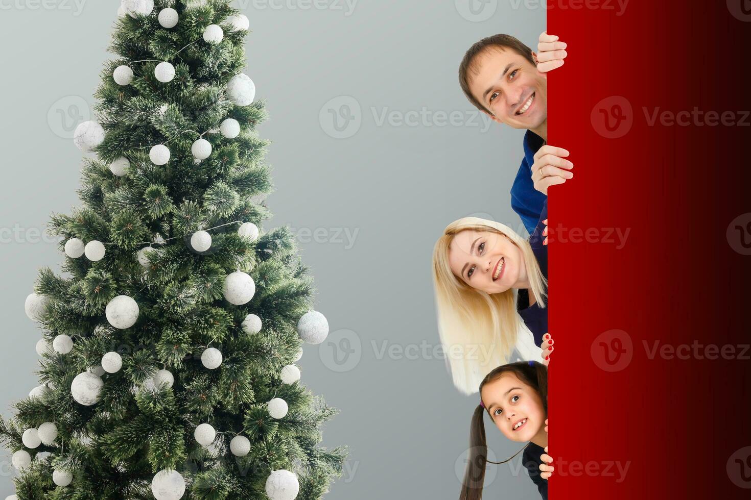 Familie späht aus Über das Weihnachten Baum dekoriert mit Spielzeuge. Familie guckt Winter Hintergrund foto