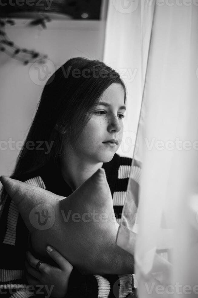 ein nachdenklich Teenager Mädchen sieht aus aus das Fenster. Nachdenklichkeit, Traurigkeit, Einsamkeit foto