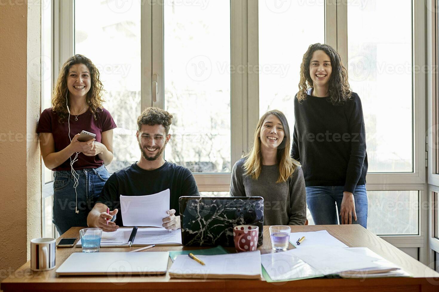 Porträt von vier glücklich Studenten beim Schreibtisch und beim das Fenster foto