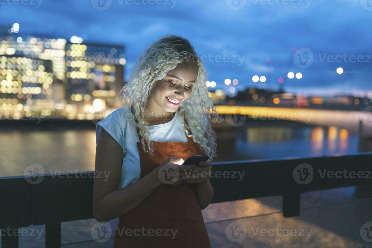 jung Frau im das Stadt beim Dämmerung suchen beim ihr Smartphone foto