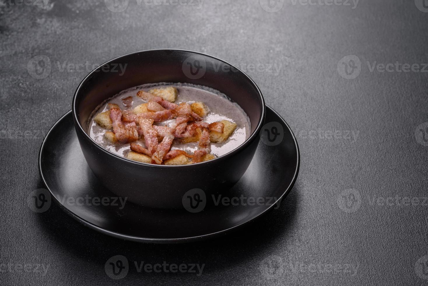 frische leckere heiße Püreesuppe mit Champignons und Speck in einem schwarzen Teller foto