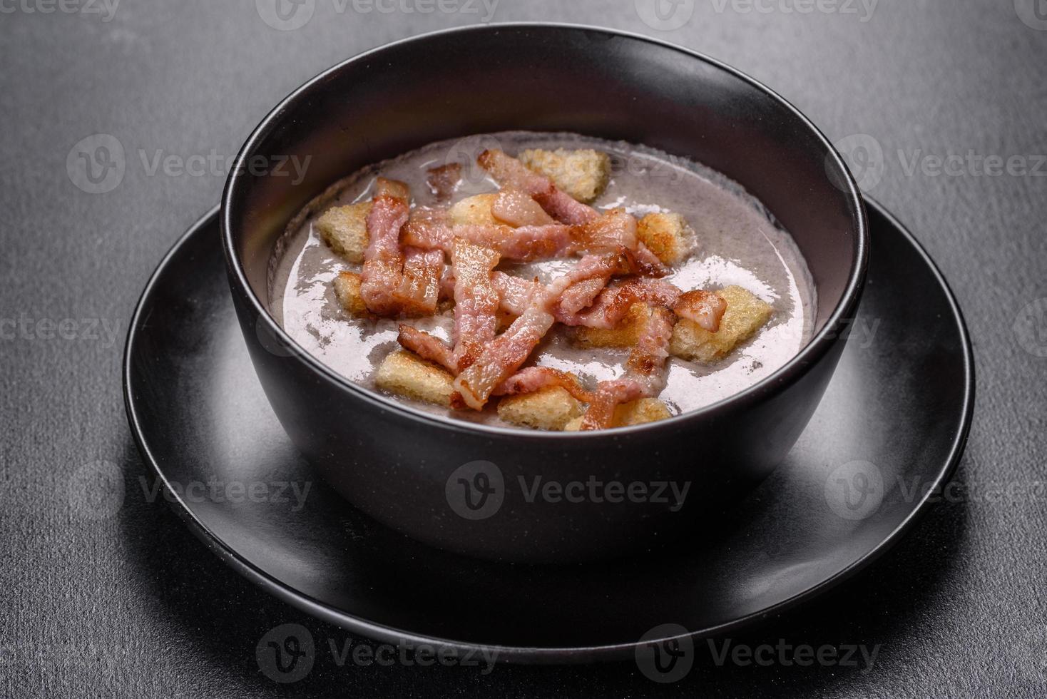 frische leckere heiße Püreesuppe mit Champignons und Speck in einem schwarzen Teller foto