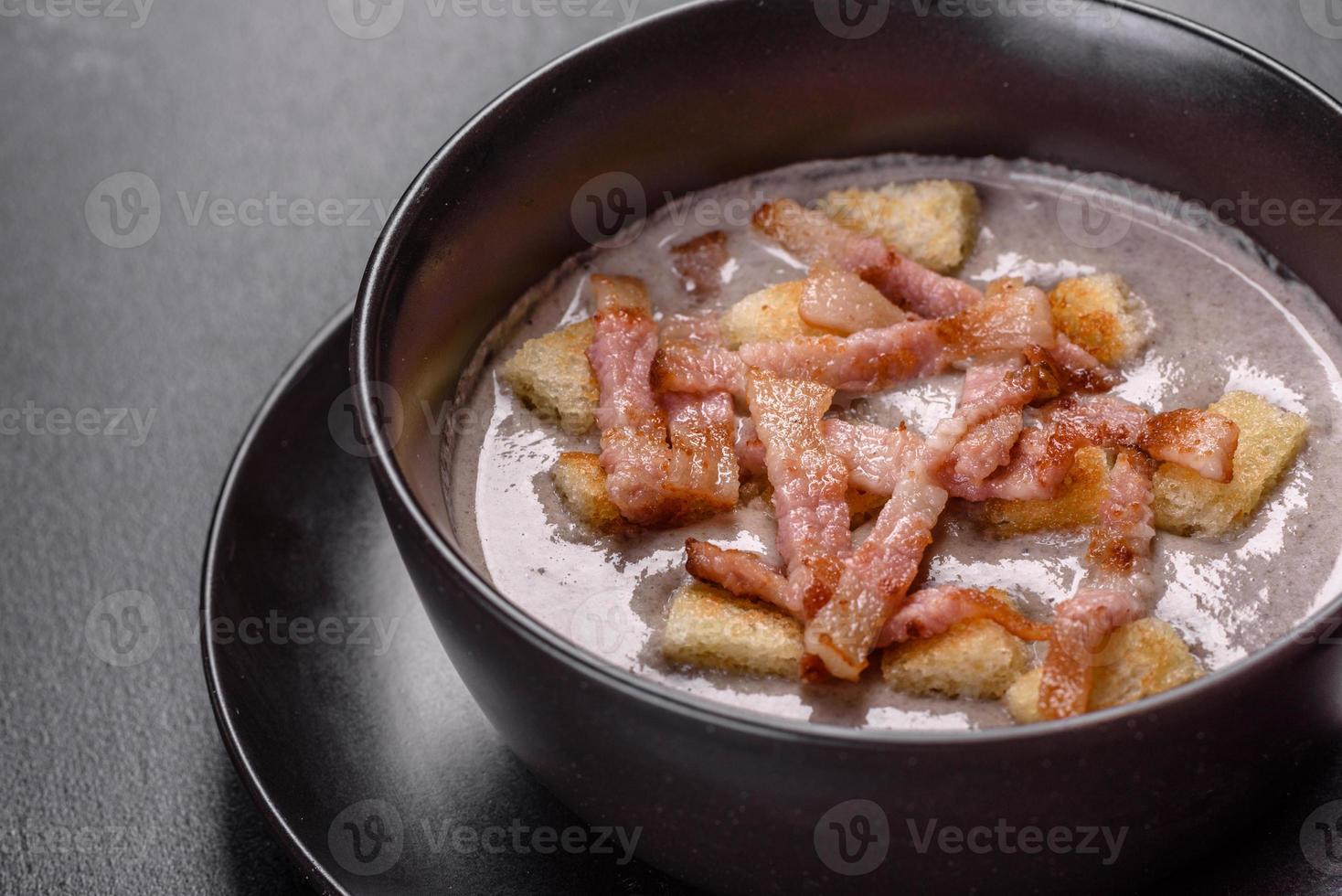 frische leckere heiße Püreesuppe mit Champignons und Speck in einem schwarzen Teller foto