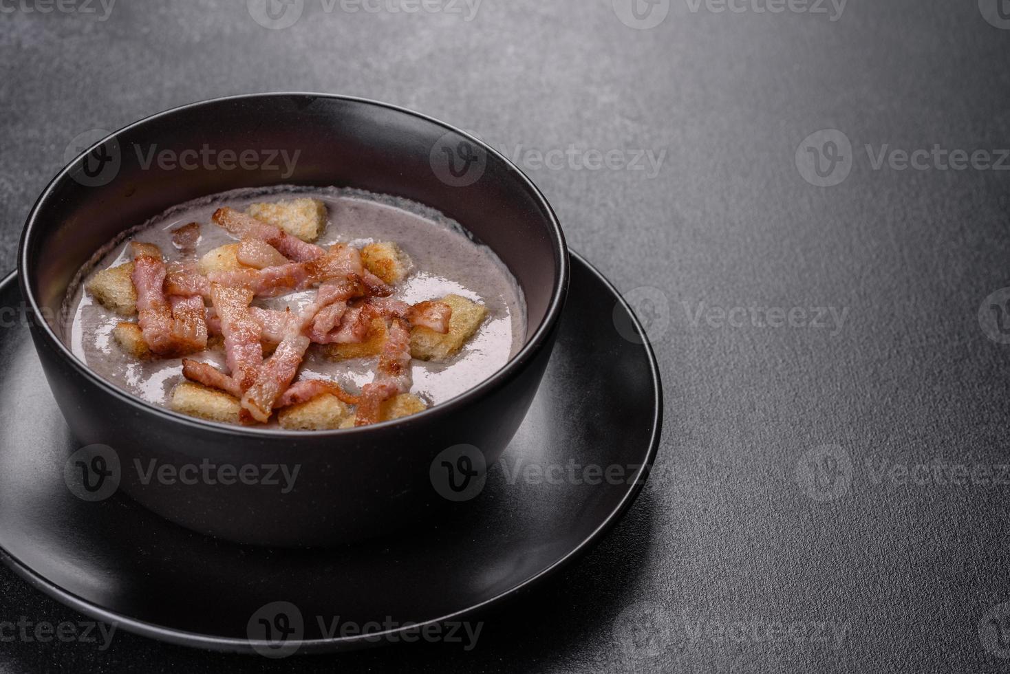 frische leckere heiße Püreesuppe mit Champignons und Speck in einem schwarzen Teller foto