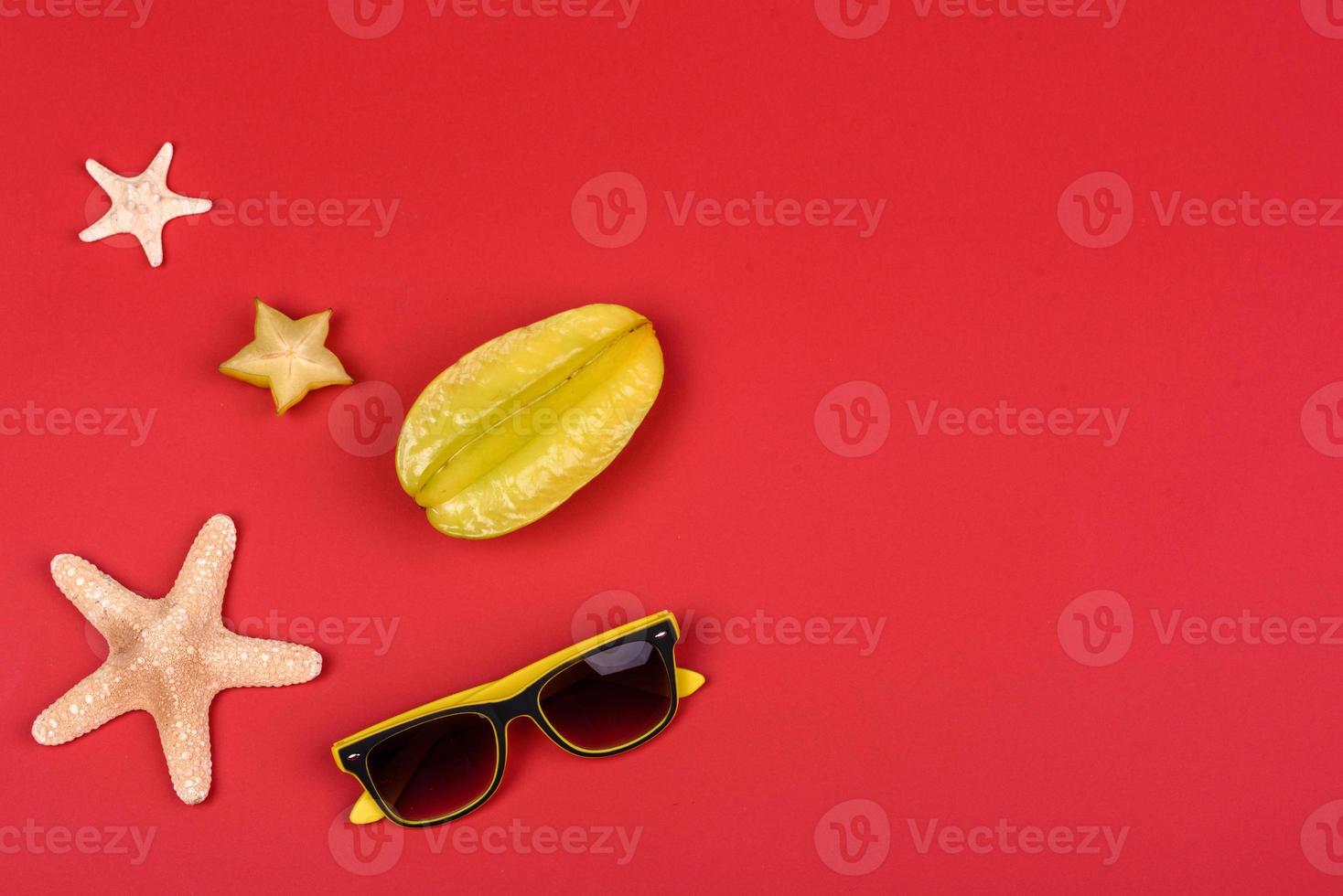 Fruchtkarambolen, Strandzubehör und Blätter einer tropischen Pflanze auf farbigem Papier foto