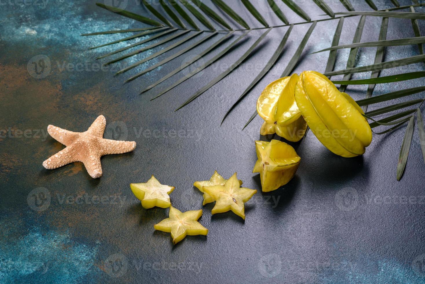 Fruchtkarambolen, Strandzubehör und Blätter einer tropischen Pflanze auf farbigem Papier foto