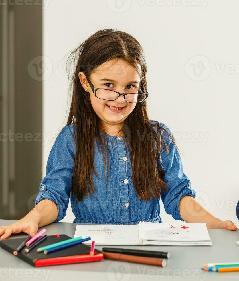 wenig Mädchen Schreiben etwas im Heft und Sitzung beim Tabelle foto