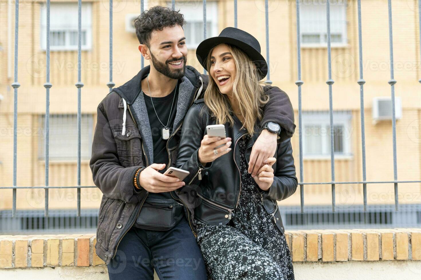 Porträt von Lachen jung Paar mit ihr Handy, Mobiltelefon Telefone im das Stadt foto