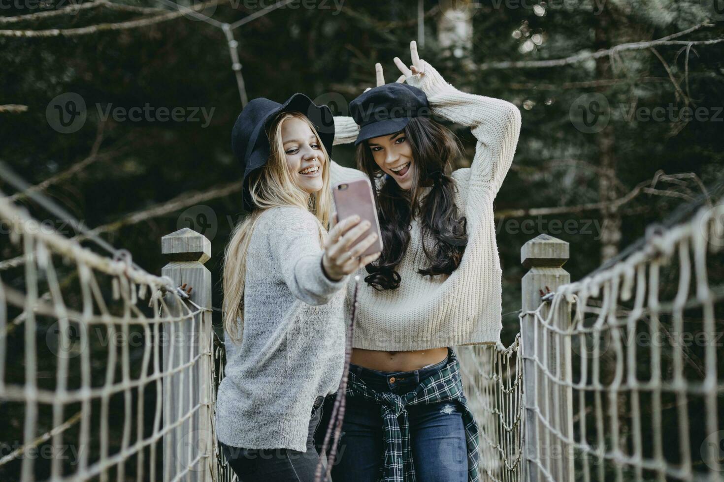 zwei glücklich jung Frauen auf ein Suspension Brücke nehmen ein Selfie foto