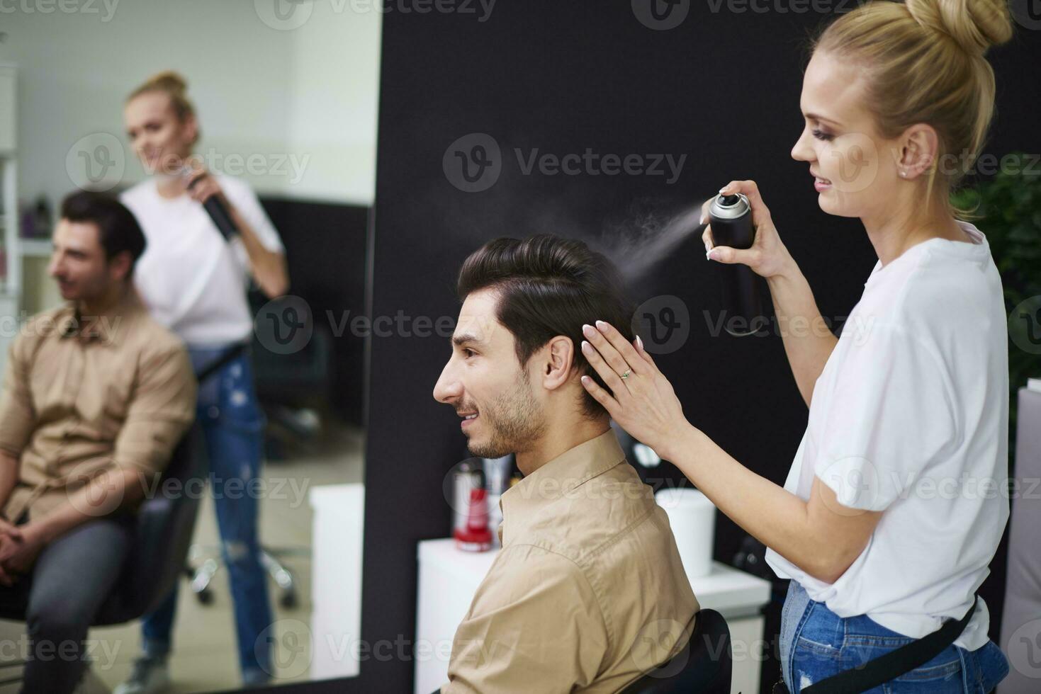 lächelnd Friseur mit Haarspray auf des Mannes Haar foto