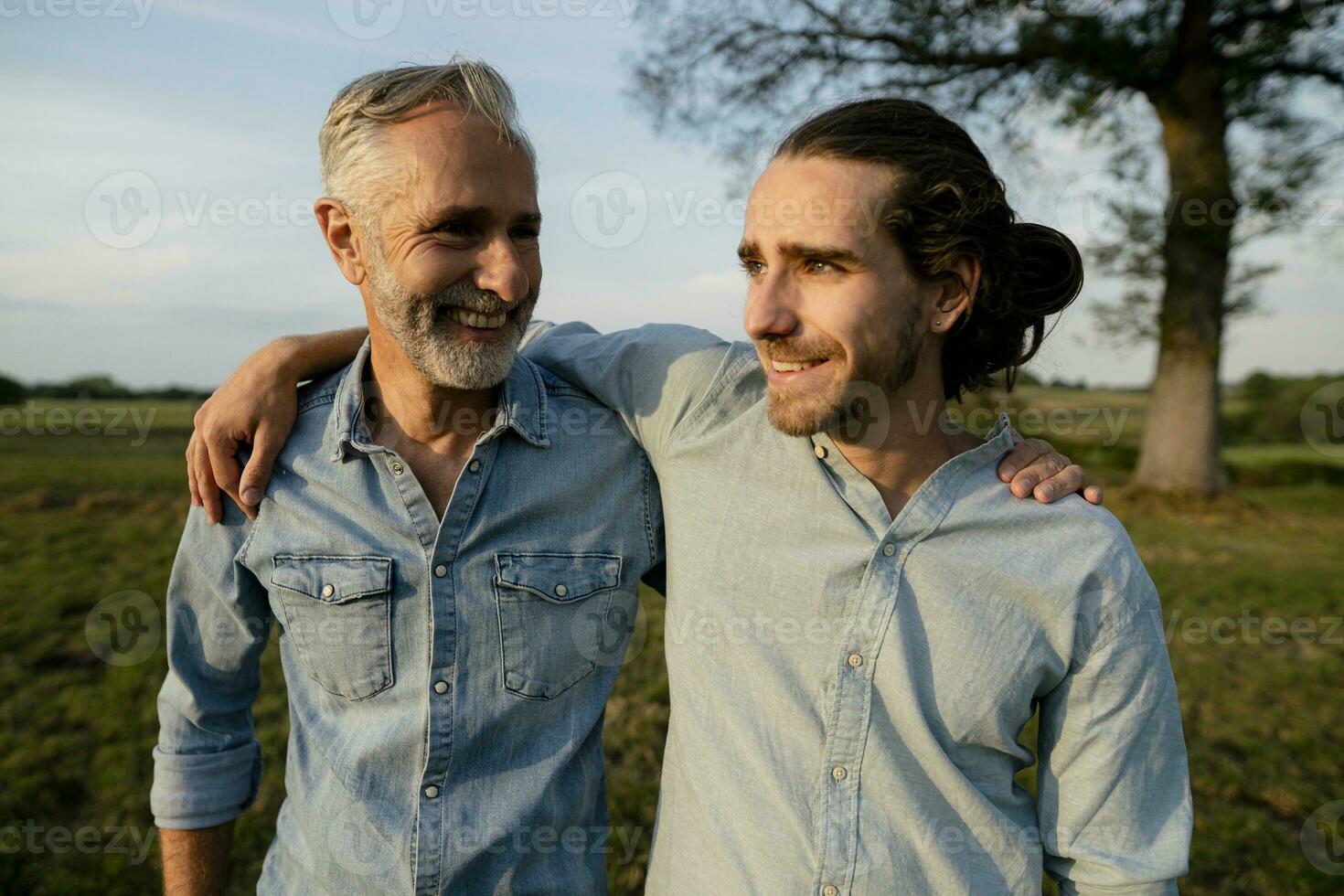 glücklich Vater und Erwachsene Sohn Umarmen auf ein Wiese im das Landschaft foto