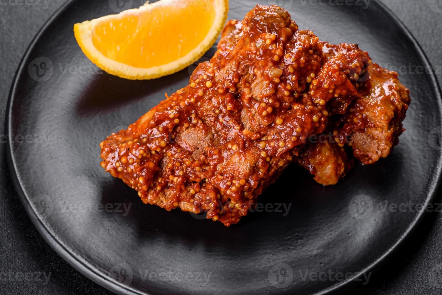 köstliche frisch gebackene Schweinerippchen mit Orange auf einem schwarzen Teller foto