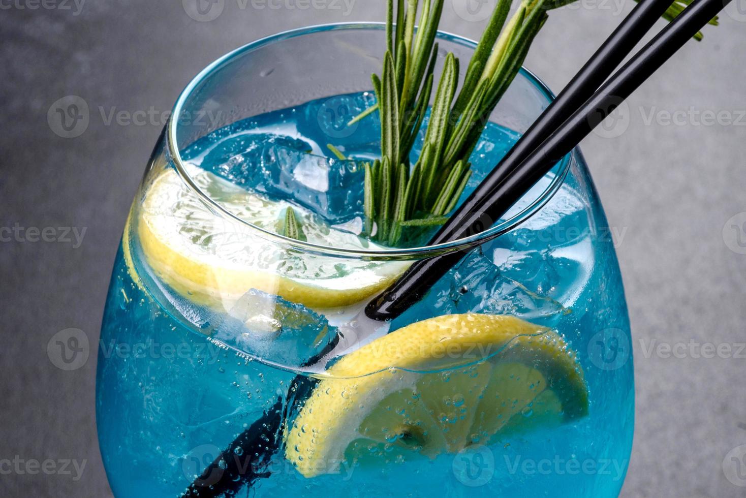 alkoholischer Cocktail Blue Curacao mit Eis, Zitrone und Cocktailröhren foto