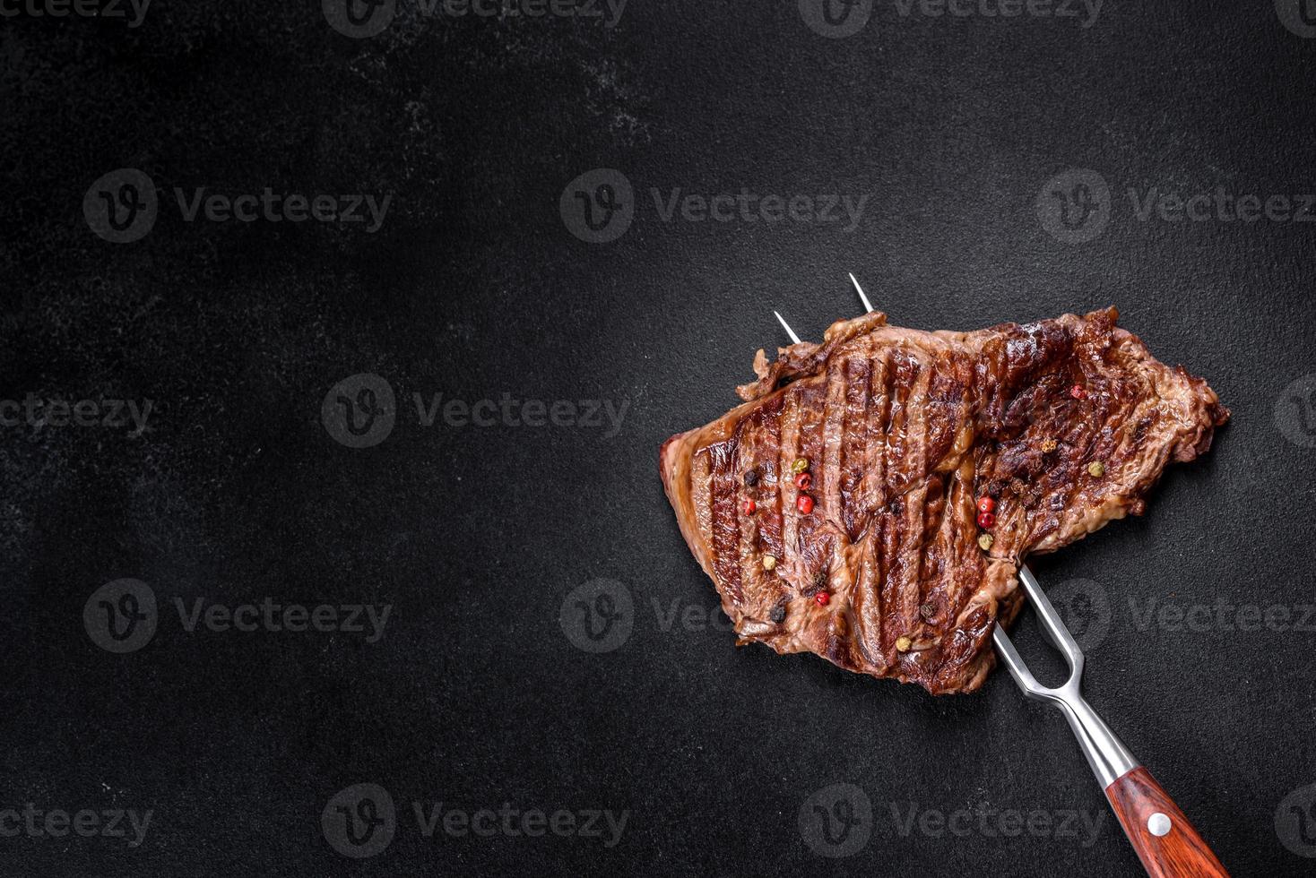 leckeres saftiges frisches Rindersteak mit Gewürzen und Kräutern auf dunklem Betongrund foto