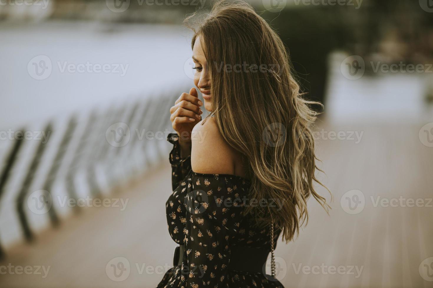 junge brünette Frau mit langen Haaren, die am Flussufer spaziert foto