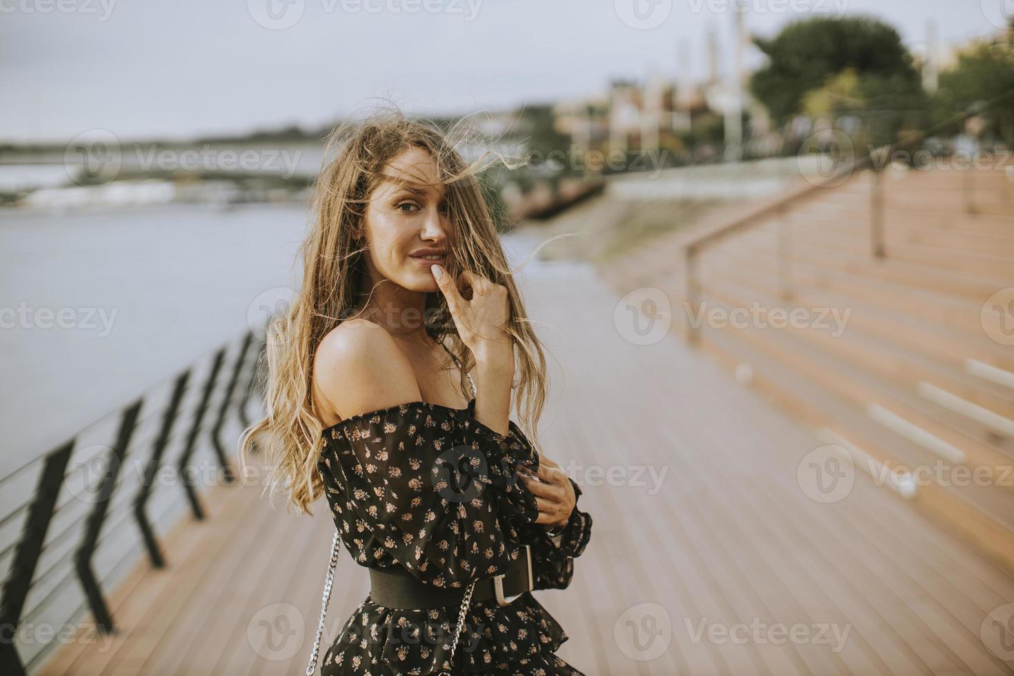 junge brünette Frau mit langen Haaren, die am Flussufer spaziert foto