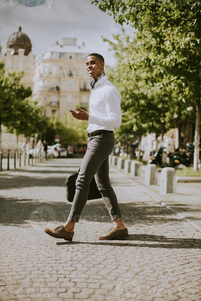 junger afroamerikanischer Geschäftsmann, der ein Mobiltelefon auf einer Straße verwendet foto