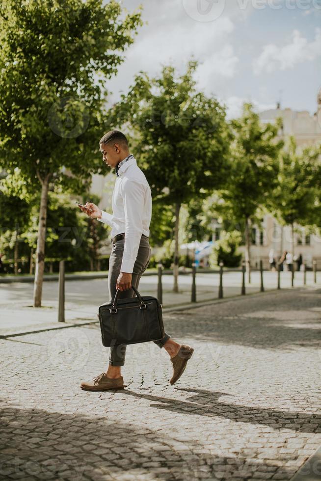 junger afroamerikanischer Geschäftsmann, der ein Mobiltelefon auf einer Straße verwendet foto