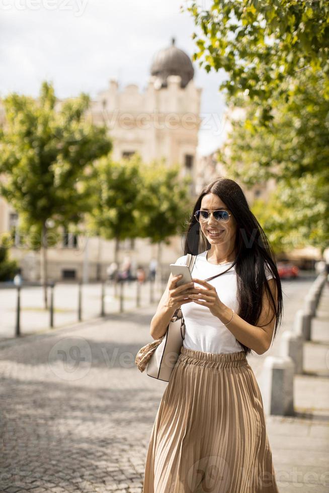 junge Frau, die ein Mobiltelefon beim Gehen auf der Straße benutzt foto