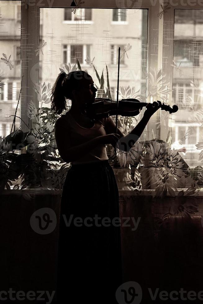 Silhouette eines jungen Mädchens, eines Musikers. Geige spielen im Hintergrund des Fensters foto