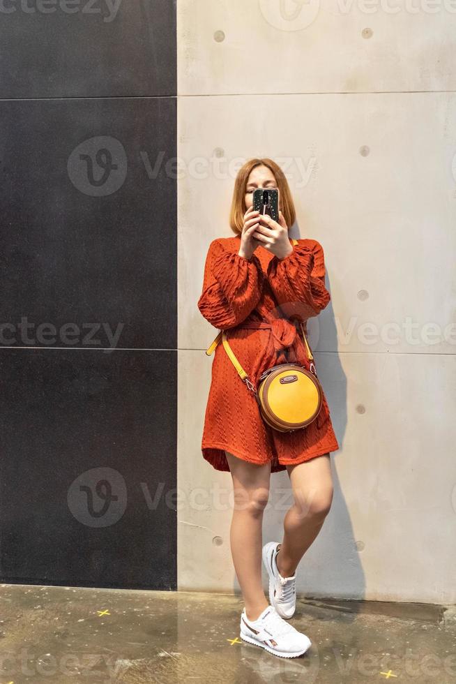 eine junge Frau in einem hellen Kleid und Turnschuhen mit einem Telefon in der Hand. mit deinem Smartphone foto