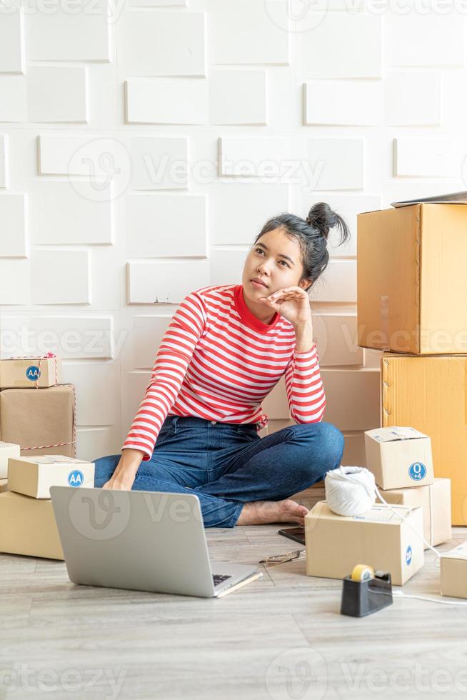 asiatische Geschäftsinhaberin, die zu Hause mit Verpackungsbox am Arbeitsplatz arbeitet - Online-Shopping-KMU-Unternehmer oder freiberufliches Arbeitskonzept foto