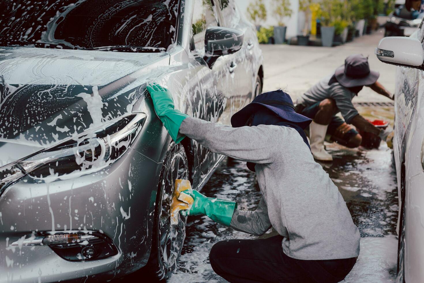 männlich Arbeiter Waschen Auto beim Auto Bahnhof draußen mit Schaum und Gelb Schwamm. foto