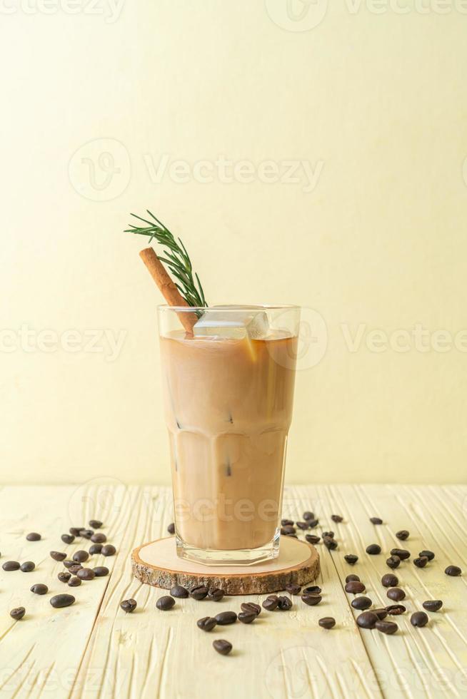 Gießen von Milch in schwarzes Kaffeeglas mit Eiswürfel, Zimt und Rosmarin auf Holzhintergrund foto