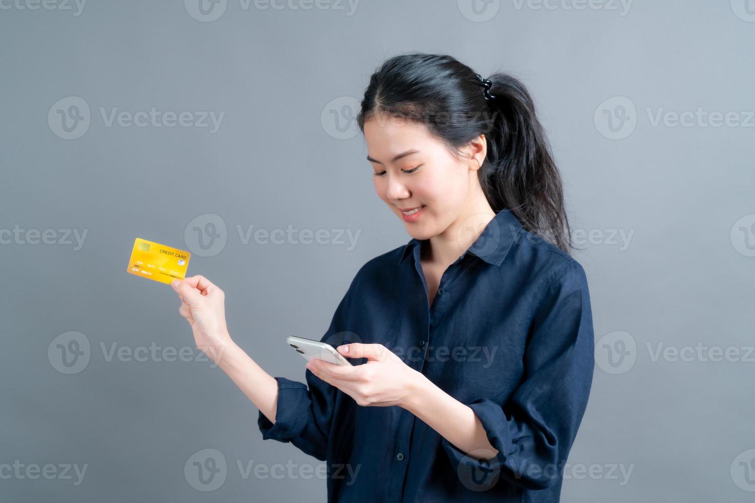 junges asiatisches mädchen, das plastikkreditkarte zeigt, während sie handy hält foto