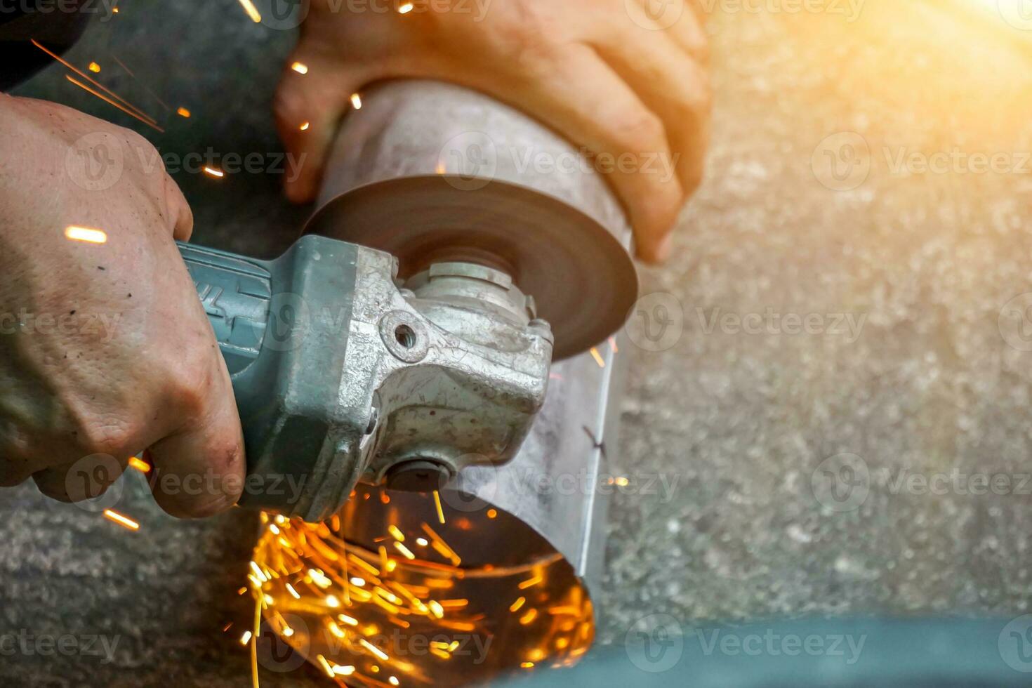 Nahansicht Hände von Arbeiter halten elektrisch Winkel Schleifer Arbeiten Schneiden verzinkt Rohr beim Konstruktion Seite? ˅ mit Sonne Fackel Hintergrund. foto