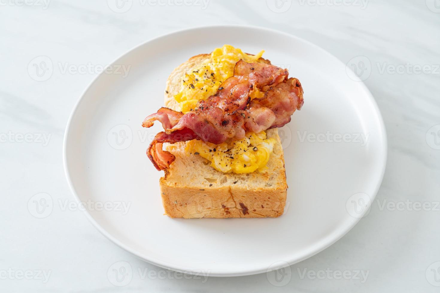 Brottoast mit Rührei und Speck auf weißem Teller foto